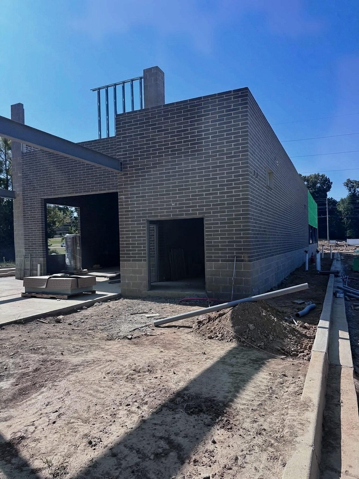 Brick shell of a new commercial building with steel canopy framing, rough-in underway at the door