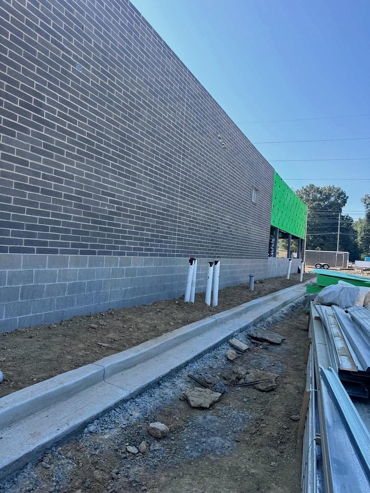 Conduit stub-ups along the base of a block wall, the curb running beside them to the far building